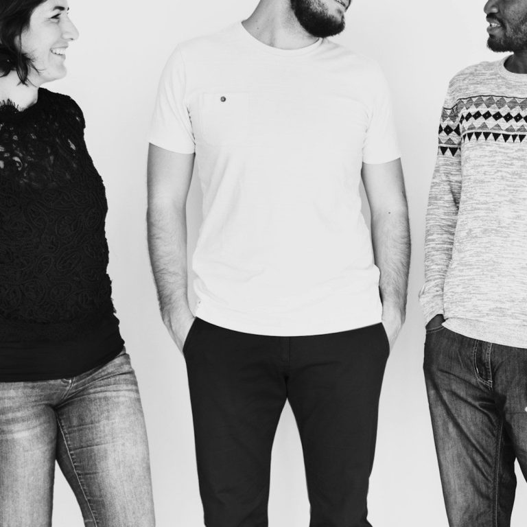 Drei Personen in legerer Kleidung, stehen in Gesprächsposition vor hellem Hintergrund.